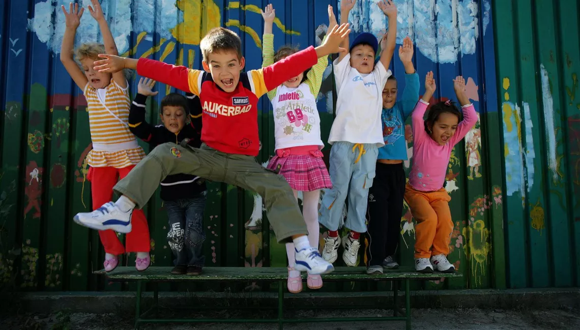  Los niños pequeños saltando en un patio de recreo en Bucarest delante de una pared con graffiti